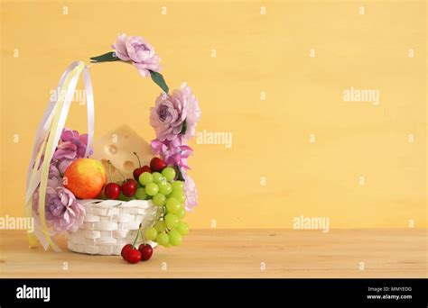 image of fruits and cheese in decorative basket with flowers over wooden table. Symbols of ...
