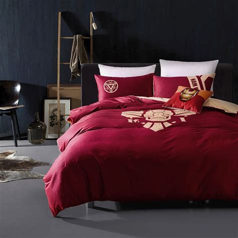a bed with red comforters and pillows in a dark colored room, next to a black chair