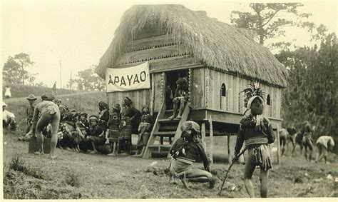 an old black and white photo of men in native garb standing near a hut