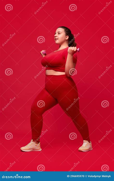 Overweight Young Beautiful Woman Training, Doing Exercises with Dumbbells Against Red Studio ...