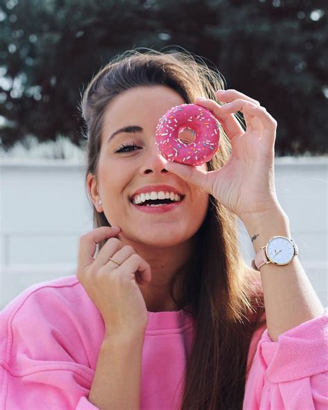 a woman holding a pink doughnut up to her eye and smiling at the camera