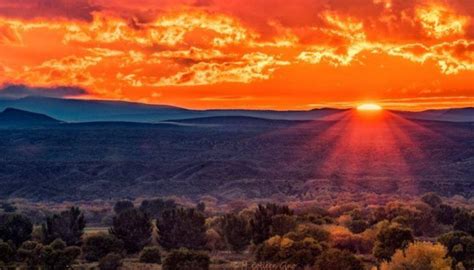 the sun is setting over mountains and trees