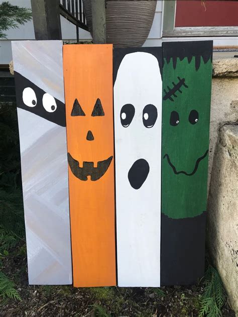 three wooden halloween signs with faces painted on them sitting in front of a house,