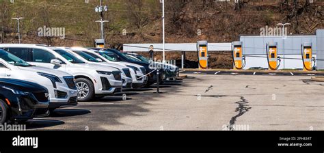 Used Cadillacs lined up for sale at a dealership in a parking lot with electric vehicle charging ...