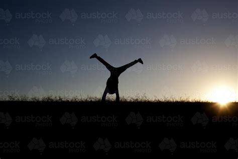 Image of Silhouette of girl doing a cartwheel at sunset - Austockphoto