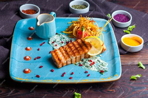 Free Photo | Side view grilled fish with garnish, lemon, sauce and spices on a blue plate on a ...