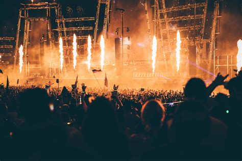 a crowd of people enjoying a concert with columns of flame on the stage ...