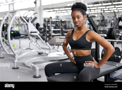 portrait of black woman taking a break after workout at gym. she sits next to barbells ...