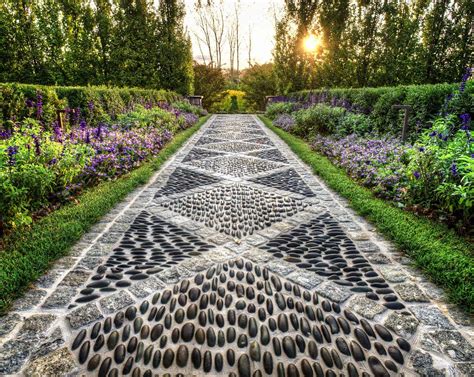 a stone pathway with stepping stones in the middle and purple flowers on either side at sunset