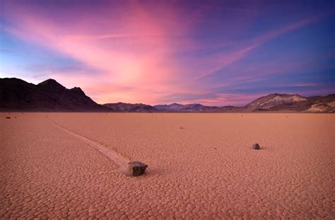 a desert landscape with rocks in the foreground and mountains in the background at sunset