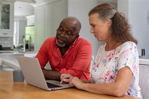 Premium Photo | Multiracial senior couple using laptop while sitting at table in living room ...