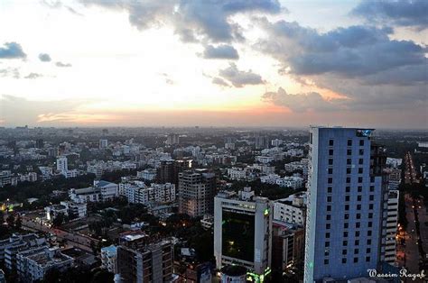 an aerial view of a city at sunset with clouds in the sky and buildings lit up