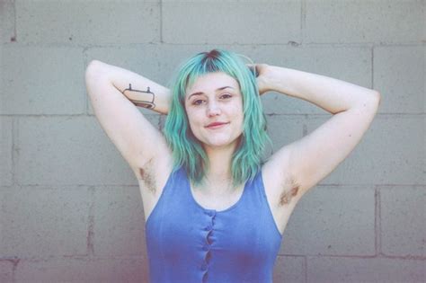 a woman with green hair and blue tank top standing in front of a brick wall