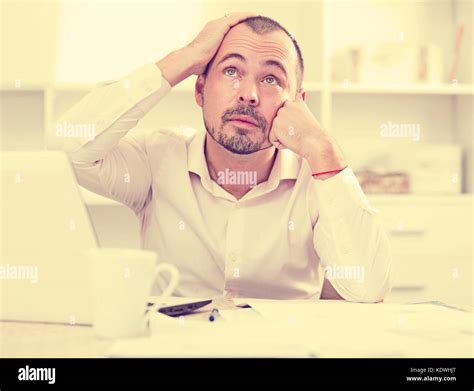 Disappointed worker at his office table feeling stressed, thinking and looking up Stock Photo ...