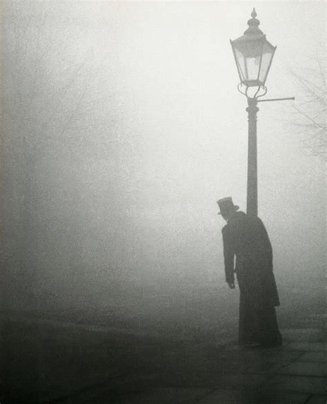 a man standing next to a street light on a foggy day in black and white