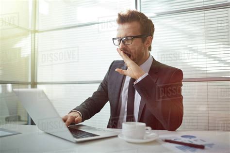 Bored yawning businessman working with laptop in office - Stock Photo - Dissolve