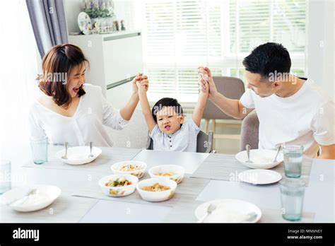 Happy Asian family raising child's hands up and smiling while having a ...