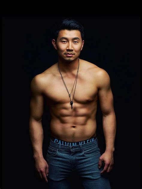a man with no shirt standing in front of a black background wearing jeans and a necklace