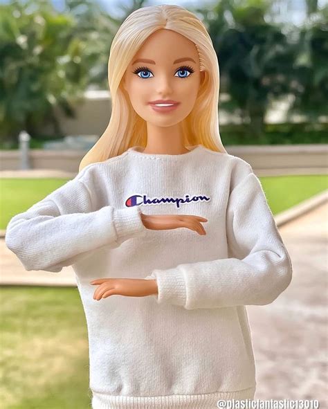 a barbie doll with blonde hair and blue eyes wearing a white sweater that says champion