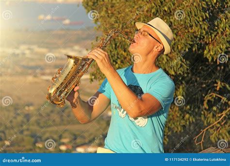 A Man in a Hat Plays Saxophone in the Nature, Against the Background of ...