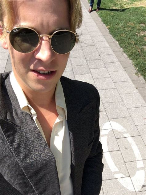 a man wearing sunglasses and a suit jacket on the sidewalk with people in the background