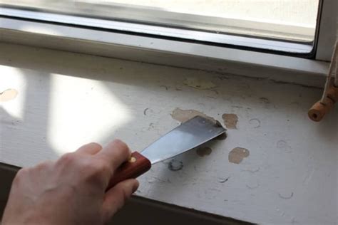 a person holding a knife near a window sill that has been torn off with tape