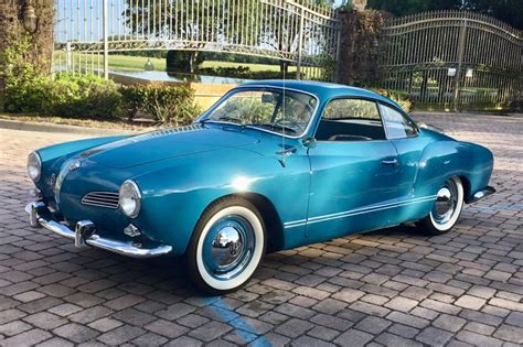 an old blue car is parked on the brick road in front of a gated area