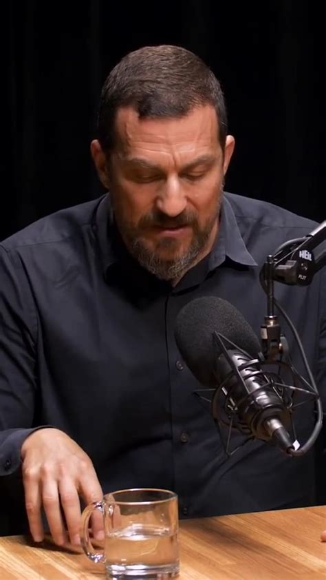 a man sitting at a table in front of a microphone with a glass of water