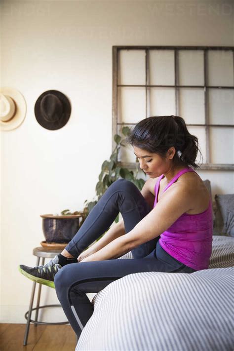 Woman wearing sports shoes while sitting on bed at home stock photo