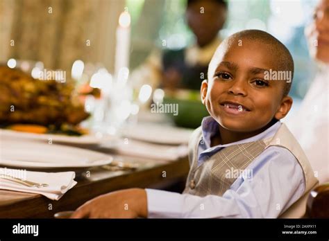 Young boy smiles as he poses for a portrait while sitting at a dining ...