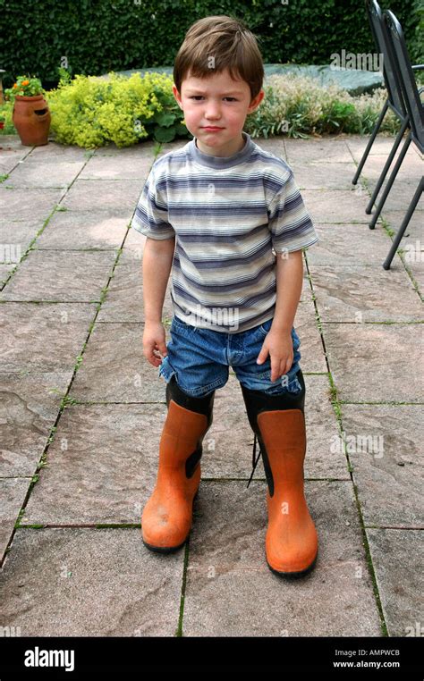 MR young boy stands on a terrasse wearing too big rubber boots Stock Photo - Alamy