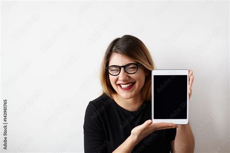 Humorous portrait of attractive young woman in glasses showing blank copy screen tablet, having ...