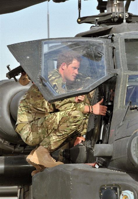 Prince Harry climbs up to examine the cockpit of an Apache helicopter ...