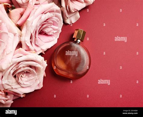 Round brown perfume bottle and pink flowers on red table. Top view. Eau de toilette. Mockup ...