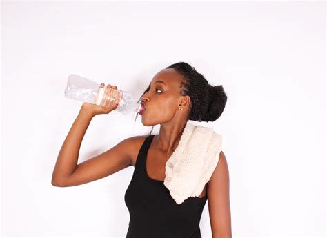 Fit woman drinking water with white towel on shoulder
