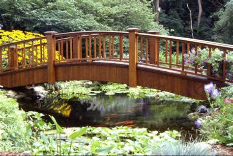 a wooden bridge over a pond filled with water lilies and other flowers in the background