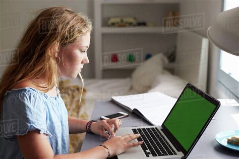 Teenage girl using laptop at a desk in her bedroom, close up - Stock Photo - Dissolve