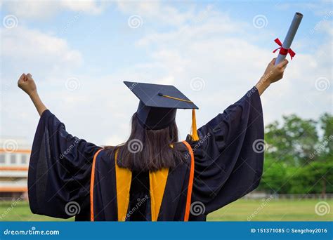 Rear View of a Female University Graduate Stands and Holds Degree Certificate To Celebrate in ...