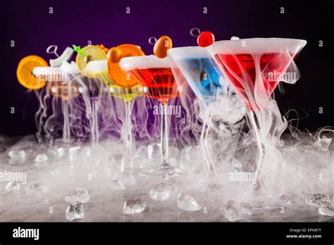 Martini drinks with dry ice smoke effect, served on bar counter with dark colored background ...