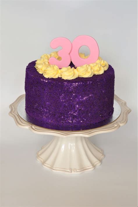 a purple cake with yellow frosting and pink number on top is sitting on a white pedestal