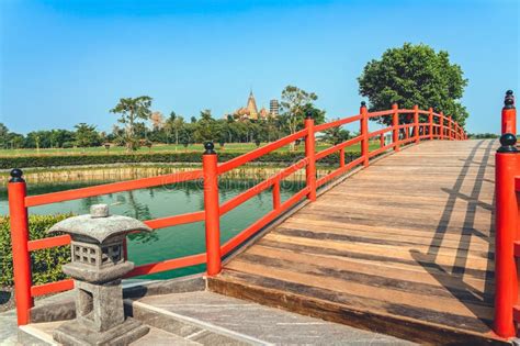 Beautiful View of Japanese Style Red Wooden Bridge Over Emerald Pond with Fountains Against ...