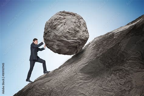 Sisyphus metaphore. Young businessman pushing heavy stone boulder up on ...