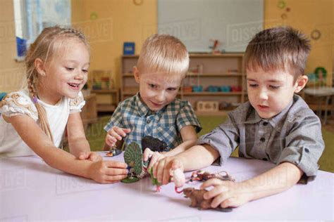 Children playing with animal toys at table in classroom - Stock Photo - Dissolve