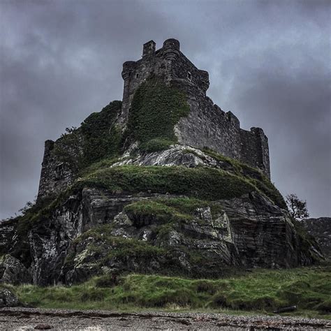 an old stone castle sitting on top of a lush green hillside under a cloudy sky