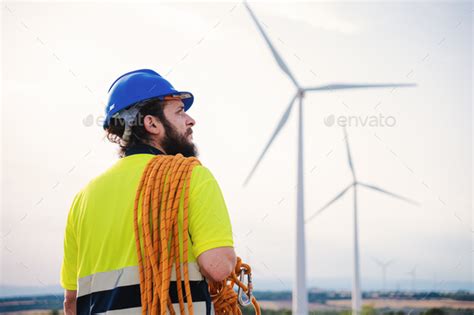 Back view of windmill turbine maintenance engineer standing wearing a hard hat nd a safety vest ...