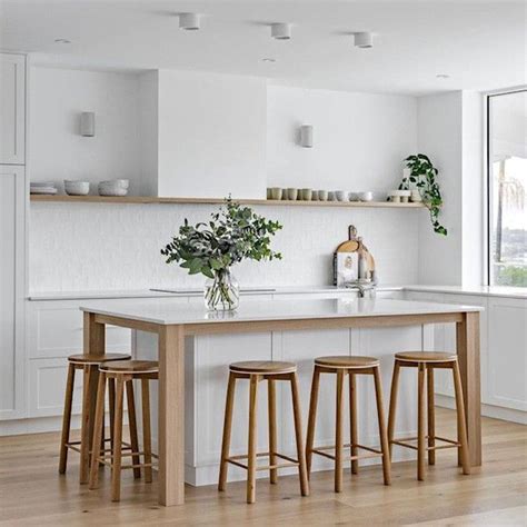 a white kitchen with wooden stools and an island in front of the countertop