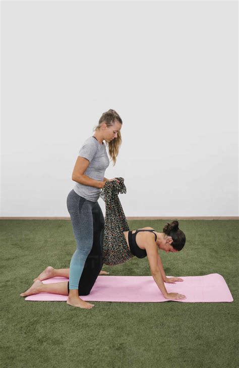 Fit pregnant woman doing cat-cow stretch exercise with female instructor at yoga studio stock photo