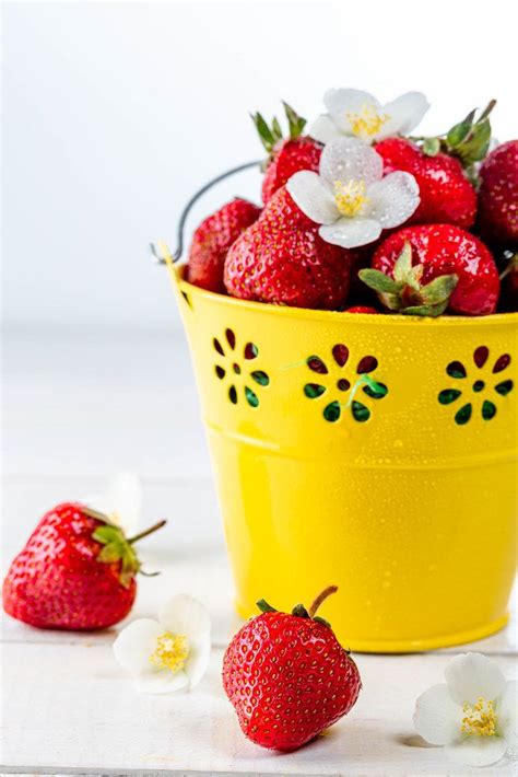 Fresh strawberries with white flowers in a yellow bucket on a wooden ...