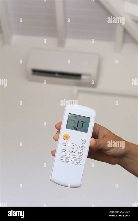 Young woman using a remote control of wall-mounted air conditioner Stock Photo - Alamy