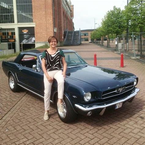 a woman sitting on the hood of a classic mustang parked in front of a building